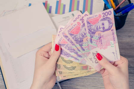 Woman's hands holding a lot of Ukrainian money over desktopの写真素材