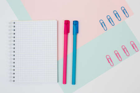 Top view photo of stationery on pink and blue background. Set of open empty spiral notepad, pens and paper clips. Minimal styleの写真素材