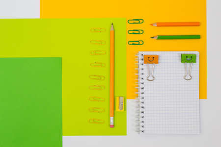 Top view positive  photo in orange, yellow and green colors of school stationery. Set of spiral notebook, pencils, clips and pencil sharpener on colorful backgroundの写真素材
