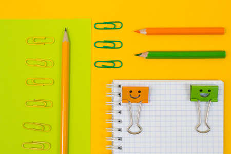 Close up top view photo of school supplies. Set of spiral notepad, clips and pencils on yellow and green backgroundの写真素材