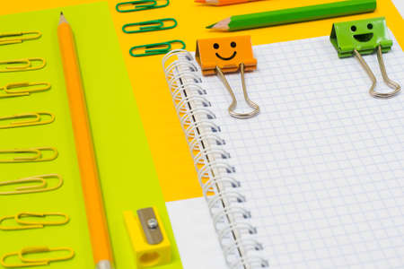 Close up top view photo of bright colorful school supplies. Set of spiral notepad, pencils, clips and pencil sharpener on orange and green backgroundの写真素材