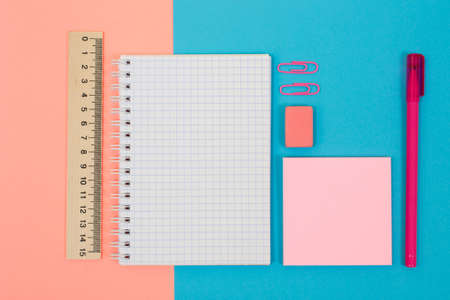 Top view photo of bright and colorful school supplies. Set of spiral notepad, pen, rubber, ruler, stickers and clips on half blue half pink backgroundの写真素材