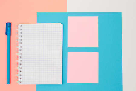 Top view photo of school supplies. Set of spiral notepad, pen and stiskers on pink and blue background. Minimal styleの写真素材