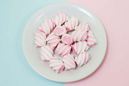 Top view photo of plate full of tasty marshmallows in the middle of half blue half pink background. Minimal style, soft colors, close up photoの写真素材