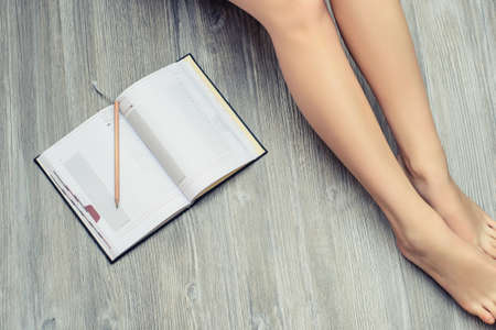Top view photo of woman's legs on wooden floor with opened diaryの写真素材