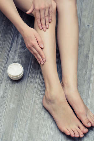 Young pretty woman applying cream on her legs in order to avoid skin irritationの写真素材
