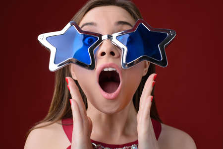 Concept of having a birthday party or xmas party. Pretty happy with big sunglasses woman inviting guests at a party, she is with open mouth and holding hands near her mouth.の写真素材