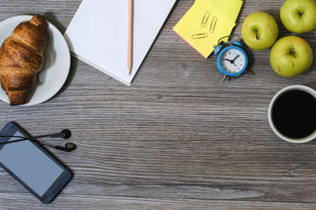 A background of office accessorise. Notepad, cup of coffee, smartphone, earphones, croissantの写真素材