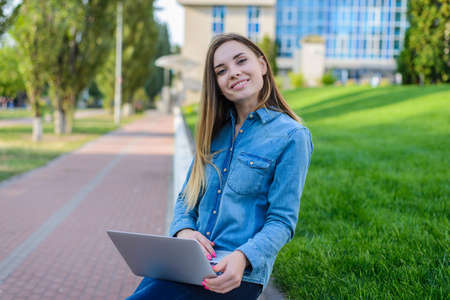 Smiling pretty woman in casual clothes with laptop on her legs is looking for neccessary information on the Internet, green grass is on the backgroundの写真素材