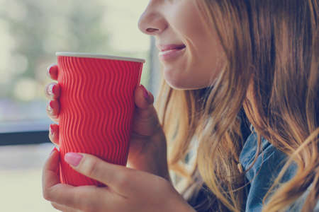 Close up cropped photo of smiling woman drinking hot fresh coffee. She is sitting in a cafe near the window and speaking with her boyfriendの写真素材