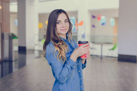 Charming smiling happy woman dressed in jeans shirt is drinking latte while doing shopping in a mallの写真素材