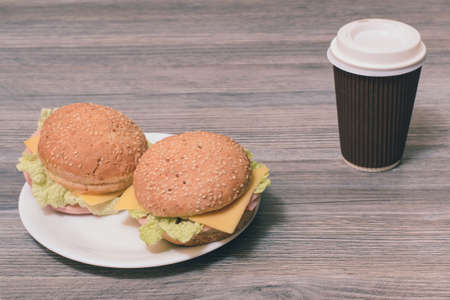 Close up photo of tasty fresh two cheeseburgers on a plate and paper cup of hot coffee on grey backgroundの写真素材