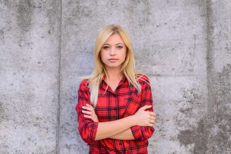Confident calm woman with crossed arms, looking at camera. Beautiful young girl in checkered red shirt standing against grey backgroundの写真素材
