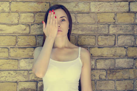 Portrait of young sad unhappy serious woman in white t-shirt closing half of her face . Brick wall on the background, vintage effectの写真素材