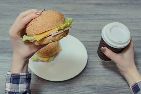 Closeup photo of hands holding burger and paper cup of coffeeの写真素材