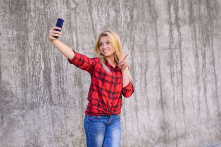 Smiling happy woman taling self-portrait using her mobile phone and showing victory sign, she wants to send this photo to her friends. It's the first time when she took a trip ro a foreign country.の写真素材