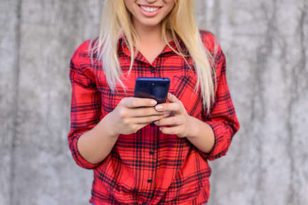 Woman using her smartphone for surfing the internet, she is watching funny videos on the internet. Young girl with beaming smile  reading sms on her mobile phone. Cropped, close up photoの写真素材