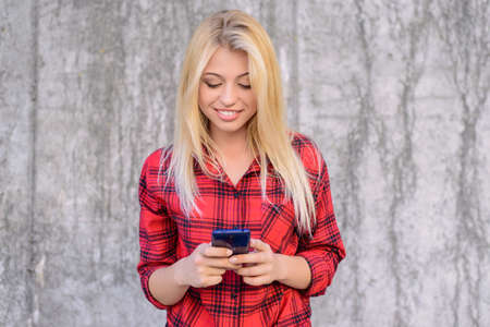 Smiling happy cheerful woman with blonde hair, in checkered shirt using mobile 3g, 4g interent for chatting and sending messages.の写真素材