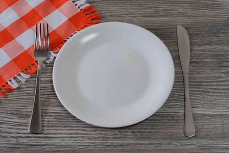Empty white round plate, knife, fork and tablecloth on  wooden table. Top view photoの写真素材