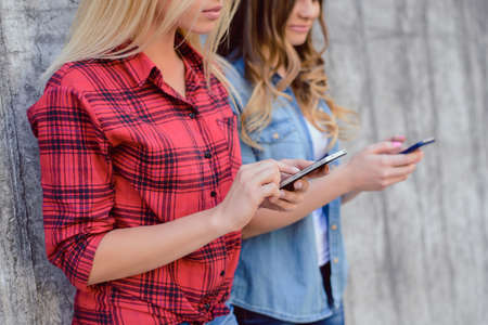 Red checkered shirt addiction lifestyle leisure rest relax social media people obsessed group outdoors teen age beauty concept. Close up photo of girls holding phones in hands isolated gray backgroundの写真素材