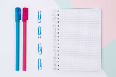 Top view photo of open empty spiral notebook, paper clips and pens on white, blue and pink background. Minimal style, close upの写真素材