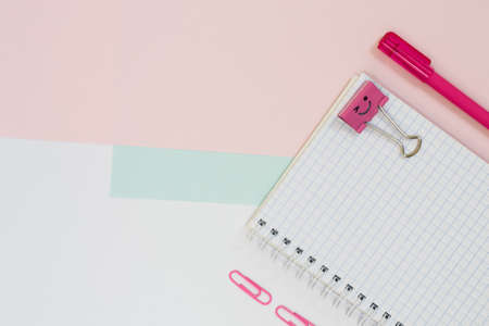 Top view photo of school supplies. Set of open spiral notebook, pen, paper clips on blue and pink backgroind. Minimal style, close upの写真素材