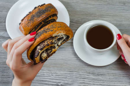 Woman has snack at work, eats roll with poppy seeds and drinks teaの写真素材