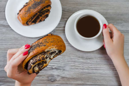 Overhead view photo of woman's hands holding bitten bun with poppy seeds and cup of coffeeの写真素材