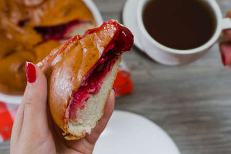 Close up photo of homemade pie with cherry filling in woman's hand and cup of tea on the backgroundの写真素材
