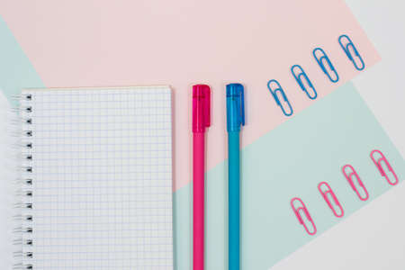 Top view photo of school supplies. Set of open spiral notepad with two pens and paper clips on blue and pink backgroundの写真素材