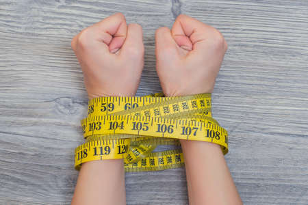 Concept of lossing weight. Woman`s hands tied with yellow tape measure.の写真素材
