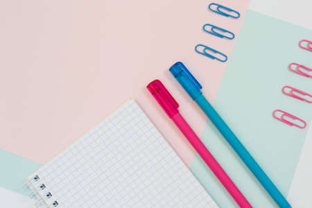 Top view close up photo of open empty spiral notepad, pens and paper clips on pink and blue baclgroundの写真素材