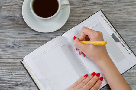 Woman writing essay in notepad at the table, cup of coffee on the background, overhead viewの写真素材