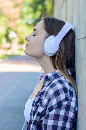 Young charming lady  in headphones listening to her favourite music in the streetの写真素材