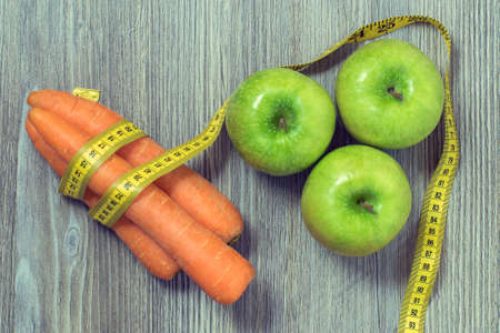 Concept of healthy nutrition. Top view photo of green fresh apples, tasty carrots and tape measure...