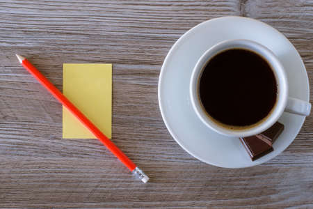 Top up overhead close up closeup photo of dark morning fresh tasty hot aromatic coffee espresso with foam yellow stickers paper for writing making notes and red pen pencil on wooden background copy-spaceの写真素材
