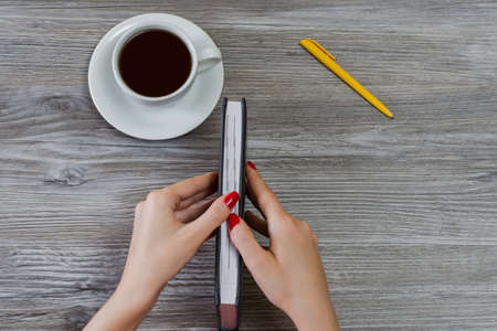 Woman's hands are trying to open closed book. Cup of coffee, a pen are on the background. Overhead viewの写真素材