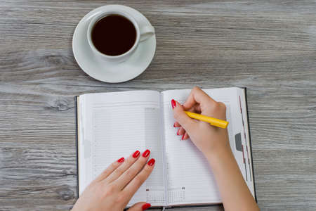Woman's hands writing information in a notepad. Cup of tea is on the background. Overhead view, copy spaceの写真素材