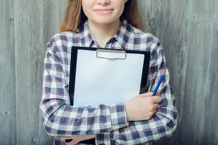 Closeup photo of woman isolated on grey wooden background holding pen and clipboard with blank paperの写真素材