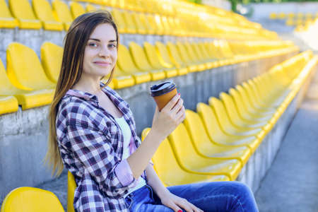 Smiling happy woman drinking coffee and watching the match at the stadiumの写真素材