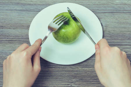 Concept of healthy eating. Close up photo of woman's hands trying to cut green fresh apple on plateの写真素材