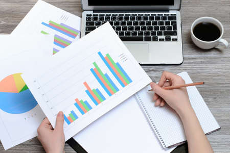 Woman's hands writing in a notepad and holding results of sales depicted on the graphicsの写真素材