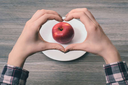 I choose healthy food!Close-up photo of woman's hands making heart frame with her fingers with apple in the center on the frame. I choose healthy food!の写真素材