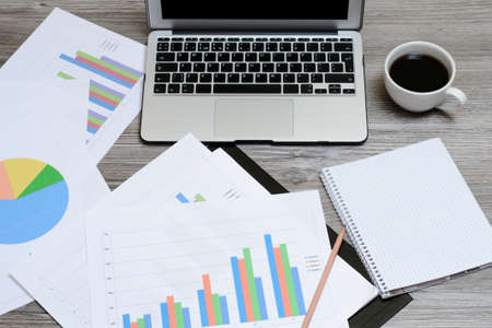 Concept of office workspace. Top view oon laptop, schemes, graphics, cup of coffeeの写真素材