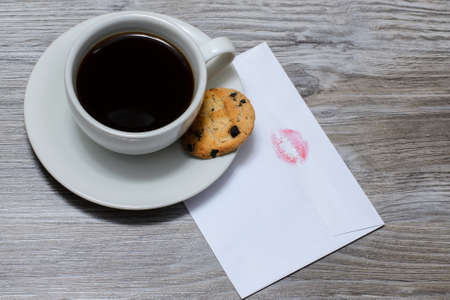 A cup of hot coffee on a saucer with a chocolate cookie, letterの写真素材