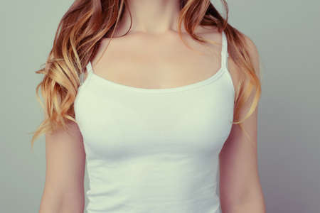 Cropped close up photo of woman's breast in white t-shirt; she has long curly hair; isolated on grey backgroundの写真素材
