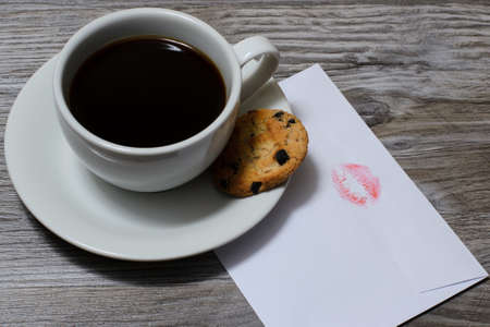 A cup of hot coffee on a saucer with a chocolate cookie, letterの写真素材