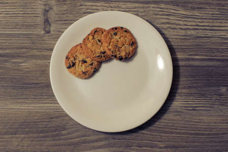 Snack breakfast crockery three cookies chocolate xmas christmas holiday homemade domestic tasty cuisine culinary cook bake bakery copy-space kitchen concept. Top over overhead view photo of fresh sweet yummy cookies on white plate isolated on dark gray wooden backgroundの写真素材