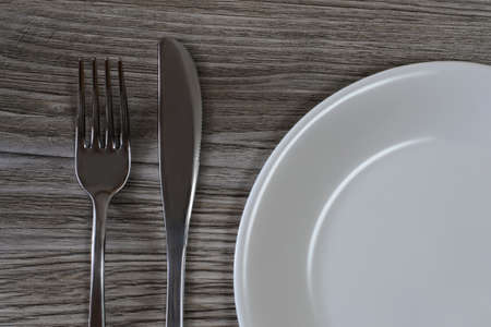 Close up photo of knife, fork and white empty plate on wooden background. Top view, cropped photoの写真素材
