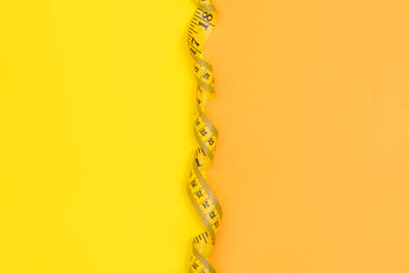 Half yellow half orange background with empty space devided with yellow tape measureの写真素材